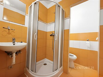 Kompaktní koupelna se sprchovým koutem, oranžová dlažba, bílá sanitární technika, moderní design, vhodná pro menší bytové prostory.