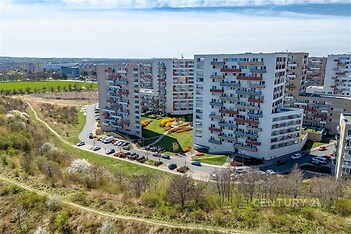 Panelový bytový komplex s moderními fasádami, obklopený zelenými plochami a parkovištěm, nabízí klidné bydlení na okraji města.