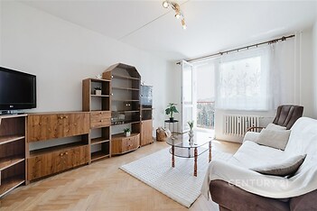 Světlý obývací pokoj s parketovou podlahou, velká okna a moderní nábytek, poskytuje příjemné posezení a propojení s balkonem.