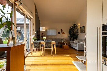 Světlý obývací pokoj s parketovou podlahou, velkými okny a moderním nábytkem. Prostorný interiér ideální pro rodinné posezení.