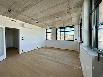 Světlý obývací pokoj s parketovou podlahou, velká okna a moderní betonový strop v rekonstruovaném bytě.