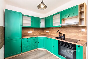 Moderní kuchyň s dřevěnou pracovní deskou, zelenými skříňkami a vestavěnou troubou. Stylový design doplňuje světlá parketová podlaha.