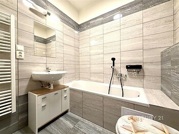 Moderní koupelna s dlažbou, vanou a umyvadlem, skříňka pod umyvadlem, koupelnový radiátor. Světlá rekonstrukce ve stylovém provedení.