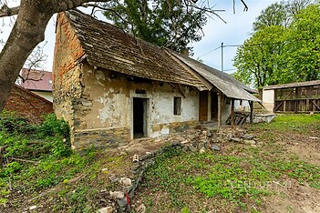 Starý venkovský dům s kamennou fasádou, dřevěnou střechou a potřebou rekonstrukce, nachází se na prostorném pozemku obklopeném zelení.