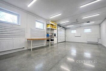 Moderní garáž s betonovou podlahou, vestavěnými policemi a úložnými prostory, světlé díky velkým oknům a dobrému osvětlení.