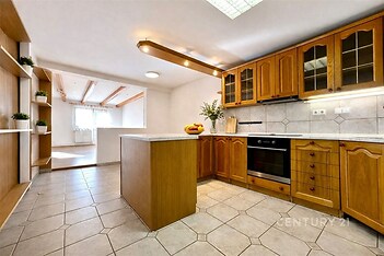 Prostorná kuchyň s dřevěnými skříňkami, dlažbou a vestavěnou troubou. Velká okna v obývacím pokoji zajišťují světlost interiéru.