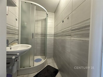 Moderní koupelna s dlažbou, sprchovým koutem a umyvadlem. Světlé keramické obklady dodávají prostoru elegantní vzhled.