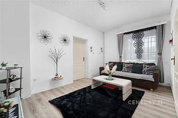 Světlý obývací pokoj s laminátovou podlahou, moderní dekorací a velkými okny poskytujícími dostatek přírodního světla.