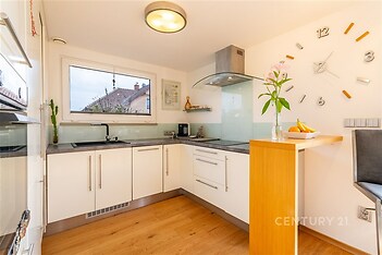 Moderní kuchyň s parketovou podlahou, světlý interiér, velká okna, moderní vybavení, dřevěné prvky, vestavěné spotřebiče, elegantní design.