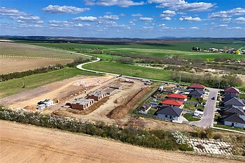 Rozestavěná obytná oblast, moderní domy s červenými střechami, okolní přírodní krajina, nedokončená stavba rodinných domů, klidná lokalita