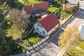 Rodinný dům s červenou střechou, obklopený zahradou, oplocený plotem. Klidná lokalita v blízkosti přírody, ideální pro rodinné bydlení.