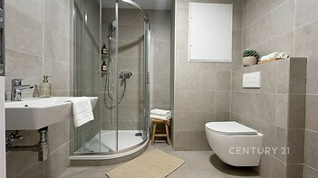 Moderní koupelna s dlažbou, sprchovým koutem a závěsnou toaletou, elegantní design a světlé provedení nabízejí komfort a styl.