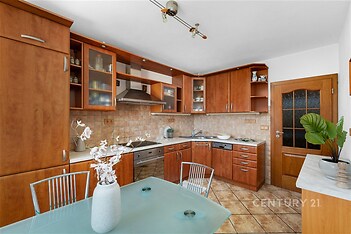 Kuchyň s dřevěnou linkou, dlažba a vestavěné spotřebiče, moderní design, světlý prostor díky velkým oknům.