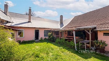 Zahrada s travnatým pozemkem u rodinného domu, s terasou a rozšířeným křídlem, vhodná pro rekonstrukci. Dominantní jsou tradiční střešní krytiny.