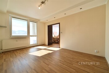 Světlý obývací pokoj s parketovou podlahou a velkými okny, moderní osvětlení, neutrální barvy, připravený k okamžitému nastěhování.