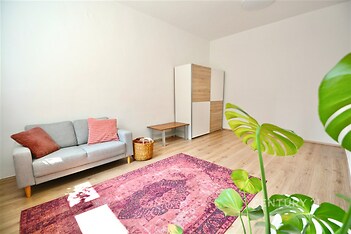 Světlý obývací pokoj s parketovou podlahou, velkými okny a moderním nábytkem, který dodává prostoru útulný a světlý vzhled.