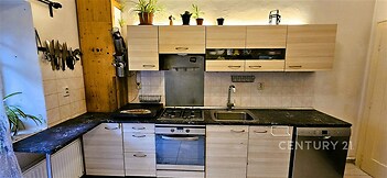 Moderní kuchyň s dřevěnými skříňkami, tmavou pracovní deskou a vestavěnou myčkou. Světlý prostor s rustikálním nádechem a praktickým uspořádáním.