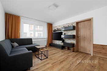 Světlý obývací pokoj, parketová podlaha, velká okna, moderní design, vestavěné police, dřevěné dveře, útulný prostor, příjemná atmosféra.