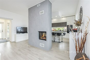Moderní obývací pokoj s krbovými kamny, parketovou podlahou a světlým interiérem, propojený s kuchyní s moderními spotřebiči.