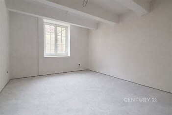 Prázdná místnost s betonovou podlahou, velkým oknem a bílými stěnami, vhodná k moderní úpravě a rekonstrukci.