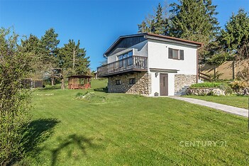 Rodinný dům s kamenným soklem a dřevěným balkónem, nacházející se na prostorném trávníku na okraji lesa, skvělý pro milovníky přírody.