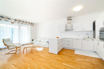 Světlý obývací pokoj s moderní kuchyní, parketová podlaha, velká okna, renovovaný interiér, bílý nábytek, otevřený prostor.