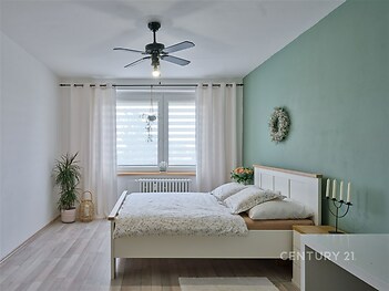 Světlá ložnice s parketovou podlahou, velkými okny a moderním nábytkem.