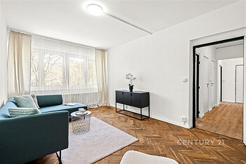 Světlý obývací pokoj s parketovou podlahou, velká okna, moderní vybavení, útulný interiér s elegantním nábytkem a výhledem do zahrady.