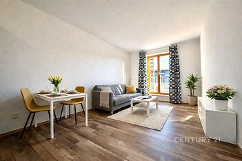 Světlý obývací pokoj s parketovou podlahou, velkými okny a moderním zařízením, poskytuje útulné prostředí k relaxaci a zábavě.