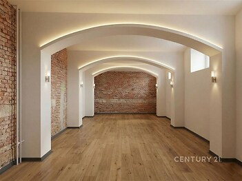 Prostorný obývací pokoj s parketovou podlahou, moderní osvětlení, cihlové zdi dodávají industriální styl, vhodný pro rekonstrukci.