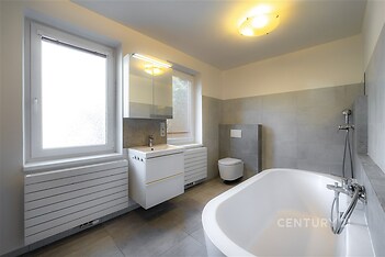 Prostorná koupelna s moderní dlažbou, velkými okny a novým osvětlením nabízí elegantní a světlý prostor k relaxaci.