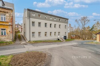 Bytový dům s moderní fasádou, situovaný v klidné ulici. Okna v pravidelném uspořádání, okolní příroda dodává příjemné prostředí pro bydlení.