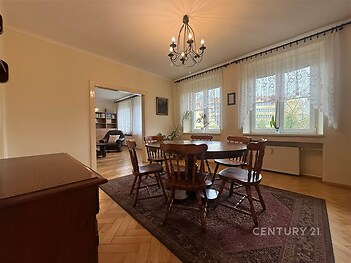 Jídelna s parketovou podlahou a velkými okny, klasický styl, dřevěný nábytek a lustr dodávají místnosti elegantní atmosféru.