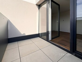 Balkon s dlažbou a velkými okny, které vedou do světlého obývacího pokoje s parketovou podlahou, moderní design a otevřený prostor.