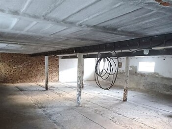 Průmyslový prostor s betonovou podlahou, cihlovou zdí a železnými nosníky, vhodný pro skladování nebo dílnu.