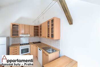 Kompaktní kuchyň s dřevěnými skříňkami, moderními spotřebiči a dlažbou, nabízí světlý prostor s vysokým stropem vhodný pro vaření.