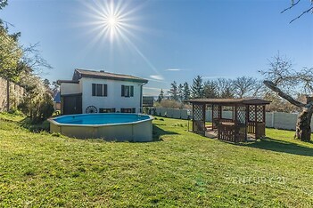 Zahradní prostor s moderním bazénem a dřevěnou pergolou, ideální pro relaxaci. Slunečné prostředí a udržovaný trávník dodávají atraktivitu.