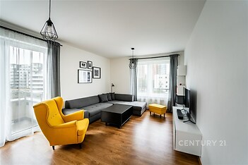 Světlý obývací pokoj s parketovou podlahou, velká okna, moderní design, pohodlná sedací souprava, žluté křeslo pro kontrast.