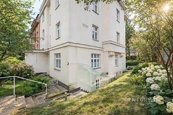 Exteriér zrekonstruovaného činžovního domu s upravenou zahradou, schodištěm a velkými okny, ideální pro klidné bydlení ve městě.