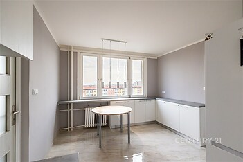 Moderní kuchyň s velkými okny, světlými skříňkami a dlažbou, nabízí prostorné uspořádání a dostatek denního světla.