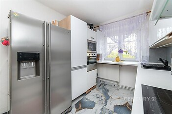 Moderní kuchyň s mramorovou dlažbou, vestavěnými spotřebiči a velkými okny, poskytujícími dostatek světla.