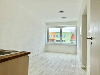 Světlý obývací pokoj s velkými okny, laminátovou podlahou a moderním designem, ideální pro útulné bydlení v rekonstruovaném bytě.