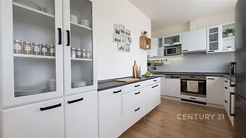 Moderní kuchyň s vestavěnými spotřebiči, parketová podlaha a bílými skříňkami nabízí světlý a organizovaný prostor pro vaření.