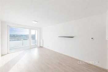 Světlý obývací pokoj s velkými okny, moderní parketovou podlahou a výhledem na prostorný balkon, přináší vzdušný a otevřený pocit.