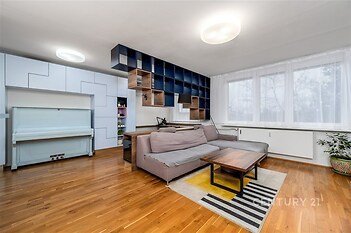 Světlý obývací pokoj s parketovou podlahou, velkými okny a moderní vestavěnou knihovnou, působí prostorně a elegantně.