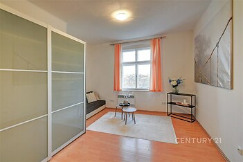 Světlý obývací pokoj s parketovou podlahou a velkými okny, moderní interiér s minimalistickým nábytkem a dekoracemi.