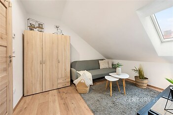 Podkrovní obývací pokoj s parketovou podlahou, střešními okny a moderním nábytkem, poskytující útulný a světlý prostor pro relaxaci.