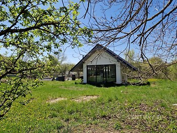 Moderní rodinný dům s velkými okny uprostřed rozlehlé zahrady, nabízí klidné prostředí a světlé prostory díky prosklené fasádě