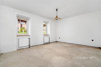 Prázdná světlá místnost, betonová podlaha, bílá výmalba, dvě okna s výhledem na zeleň, příprava na rekonstrukci, ideální pro modernizaci