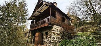 Dřevěná chata s kamennou podezdívkou, obklopená lesem, nabízí klidné prostředí. Rustikální design s balkónem a výhledem na přírodu.